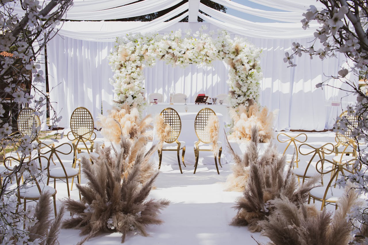 Beautifully decorated outdoor wedding setup with chairs and floral arch under a white canopy.