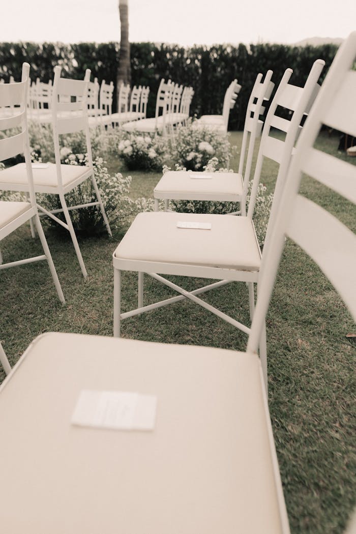 A serene setup for an outdoor wedding ceremony with white chairs and floral decor.