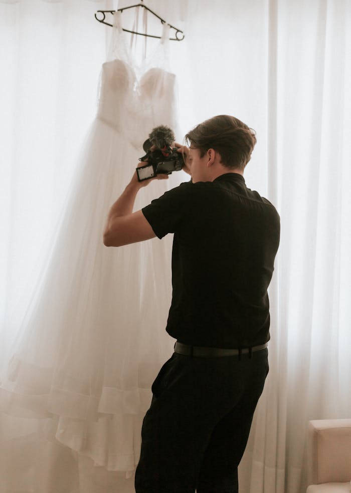 A photographer takes a picture of a hanging bridal gown in natural lighting.