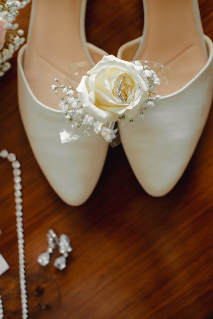 contact-img Close-up of bridal shoes adorned with a white rose beside elegant jewelry.