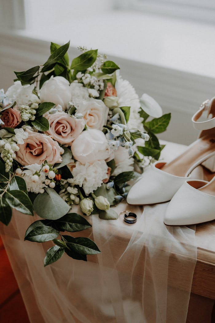 Chic floral bouquet with bridal shoes and wedding rings, symbolizing a romantic wedding setting.