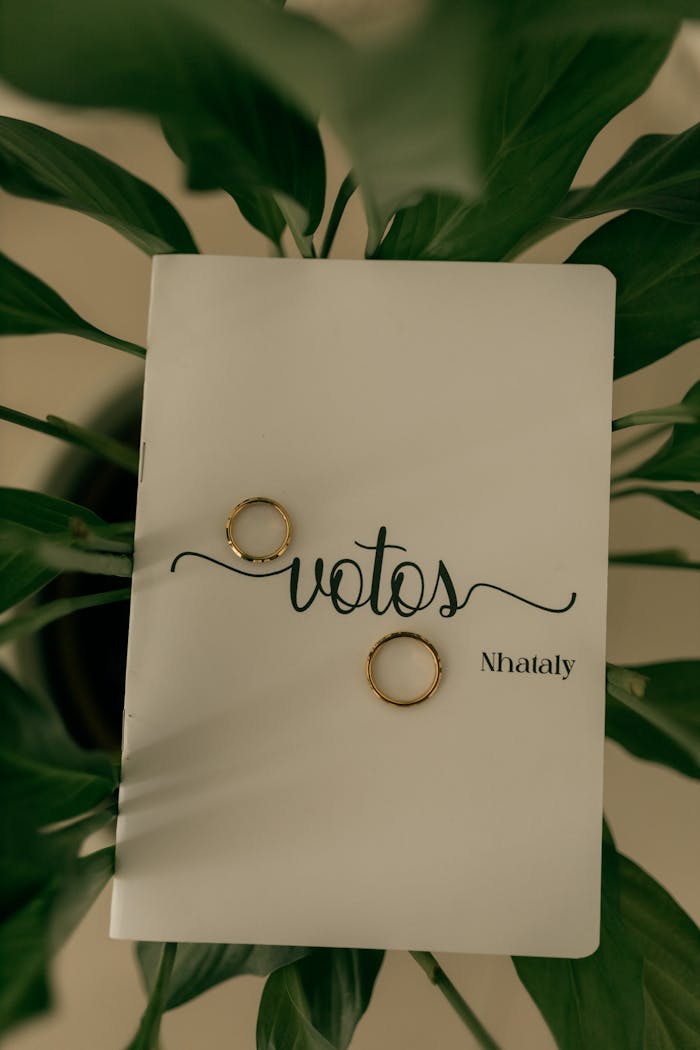 Elegant wedding vows book with gold rings, surrounded by lush green leaves, perfect for romantic ceremonies.